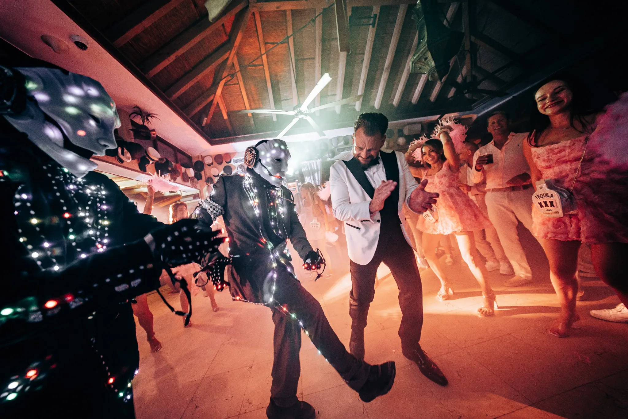 Performers in illuminated costumes dancing with guests at an evening party