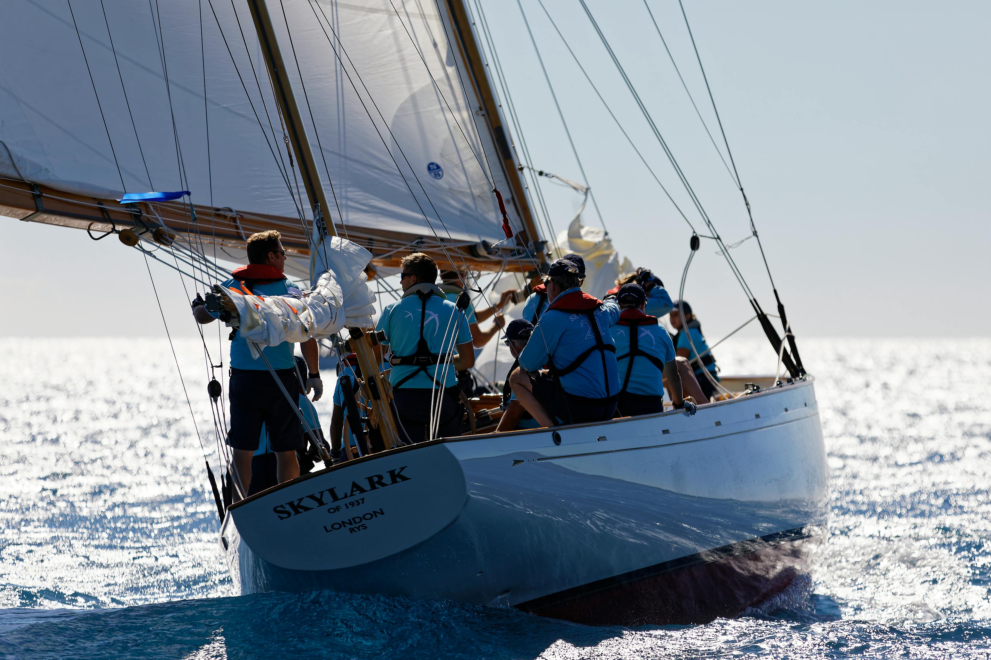 A team in matching shirts and life vests sailing a classic wooden yacht